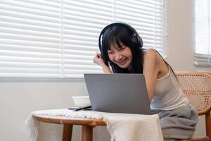 Young woman using laptop computer and wearing headphone at home photo