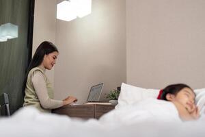 Asian mother working on bed with sleeping daughter by side at home photo