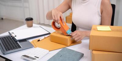 Woman asian use scotch tape to attach parcel boxes to prepare goods for the process of packaging, shipping, online sale internet marketing ecommerce concept startup business idea photo