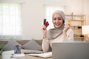 Young woman using laptop at home shopping online. Muslim woman wearing hijab using laptop and holding credit card. Internet banking concept. Muslim woman online shopping photo