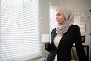 negocio mujer musulmán. confidente mujer de negocios musulmán en hijab en pie con Mañana café jarra en oficina foto