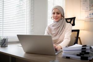 asiático musulmán mujer de negocios en hijab cabeza bufanda trabajando con papel documento en el moderno oficina. diversidad y oficina concepto foto