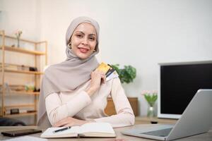 Young woman using laptop at home shopping online. Muslim woman wearing hijab using laptop and holding credit card. Internet banking concept. Muslim woman online shopping photo