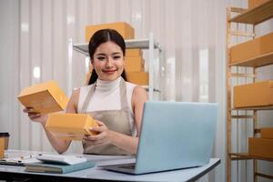 joven negocio mujer asiático trabajando en línea comercio electrónico compras a su tienda. joven mujer vender preparar paquete o empaquetar caja de producto para entregar a cliente. en línea de venta foto