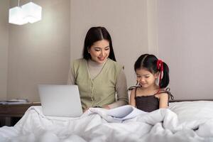 Mom work from home with children. Mother working on bed laptop in bedroom with child daughter. Funny authentic lifestyle family moment photo