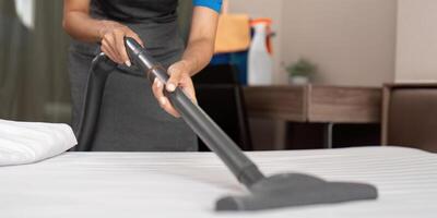 Cleaning service employee removing dirt from with professional equipment. Female housekeeper cleaning the mattress on the bed with vacuum cleaner photo