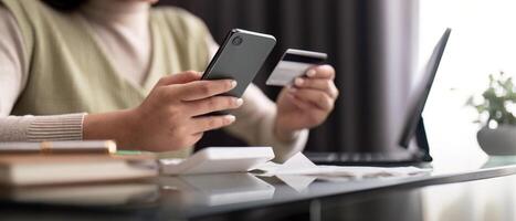 joven mujer participación móvil teléfono y crédito tarjeta sentado a el mesa. contento mujer hace en línea compras utilizando móvil pago. bancario aplicación Servicio foto