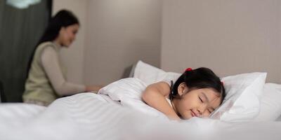 Asian mother working on bed with sleeping daughter by side at home photo