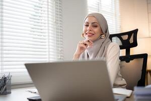 asiático musulmán mujer de negocios en hijab cabeza bufanda trabajando con papel documento en el moderno oficina. diversidad y oficina concepto foto