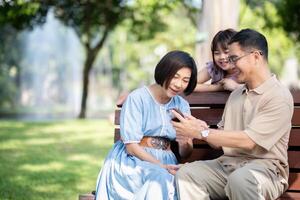 Family, generation and technology concept happy smiling grandmother, grandfather and little granddaughter with telephone sitting at park photo