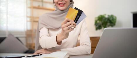 Young woman using laptop at home shopping online. Muslim woman wearing hijab using laptop and holding credit card. Internet banking concept. Muslim woman online shopping photo