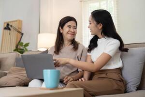 Mother and beautiful young grownup daughter using online app on laptop, watching movie, interactive TV channel. spending leisure time together at home photo