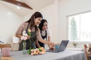 mayor madre y adulto hija contento en el mesa mientras organizar flores en un florero juntos utilizando ordenador portátil computadora. estilo de vida concepto. contento hora juntos foto