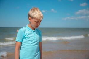 Handsome teenager boy of European appearance with blond hair in a blue T-shirt, and white shorts,stands behind blue sky, and looks thoughtfully to down. Summer vacation concept.Handsome teenager boy portrait concept.Copy space. photo