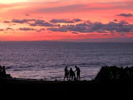 a family is standing on the edge of a cliff overlooking the ocean at sunset photo