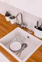 White plates, glass glasses and forks in a clean white sink on a wooden table in a white kitchen photo