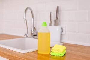 White plates, glass cups and forks in a clean white sink and two bottles of detergent and microfiber rags on a wooden table in a white kitchen photo