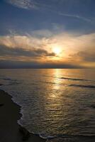 Sunset, illuminated sea. Sandy beach in the foreground. Light waves. Baltic Sea photo