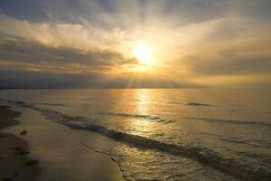 Sunset, illuminated sea. Sandy beach in the foreground. Light waves. Baltic Sea photo