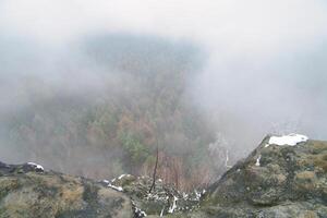 View from the large Zschirnstein into the valley of colorful conifers through fog photo