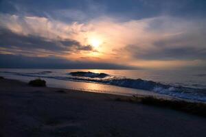 Sunset, illuminated sea. Sandy beach in the foreground. Light waves. Baltic Sea photo