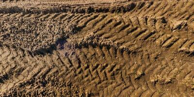 ver desde encima en textura de mojado lodoso la carretera con tractor neumático pistas en campo foto