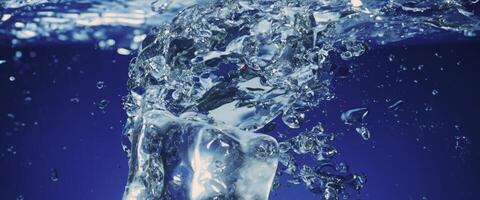 agua salpicaduras y hielo cubo. hielo salpicaduras dentro un vaso de agua. submarino torrencial hielo cubitos que cae dentro claro riego antecedentes. refrescante frío Bebiendo. helados en un vaso con azul antecedentes foto