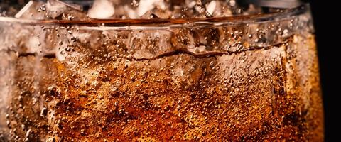 Splashing of Cola and Ice. Cola soda and ice splashing fizzing or floating up to top of surface. Close up of ice in cola water. Texture of carbonate drink with bubbles in glass. Cold drink background photo