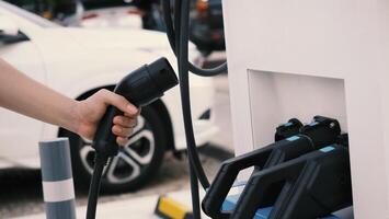 mano participación ev cargando enchufe en frente de cámara con borroso antecedentes de exterior. conductor de eléctrico coche sostener baterías cargador enchufar. sostenible energía motorizado eléctrico cargando estación antecedentes foto