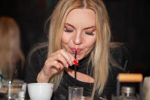 A beautiful middle-aged blonde drinks a cocktail through a straw. photo