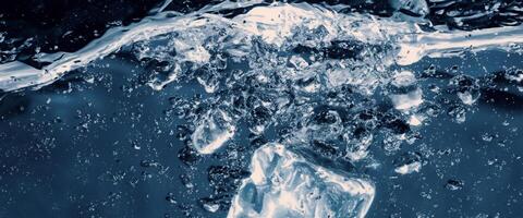 agua salpicaduras y hielo cubo. hielo salpicaduras dentro un vaso de agua. submarino torrencial hielo cubitos que cae dentro claro riego antecedentes. refrescante frío Bebiendo. helados en un vaso con azul antecedentes foto