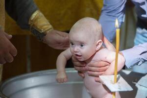 ortodoxo bautismo de un niño. baños un bebé en un Iglesia fuente cuando aceptar fe. foto