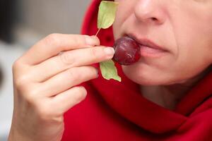 A woman, whose face is not visible, eats a small red wild apple. photo