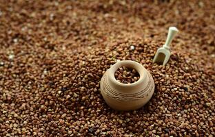 Background image of a large pile of buckwheat, in the middle of which lies a small jug and a wooden spatula for cereals photo