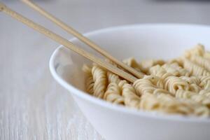 Bowl of instant cooking noodles with wooden chopsticks on white wooden table photo