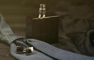 A bottle of mens cologne and cufflinks with blue tie lie on a black luxury fabric background on a wooden table. Mens accessories photo