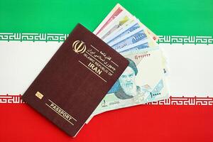 Red Islamic Republic of Iran passport and iranian reals money bills background close up photo