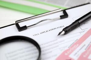 Typical Visa application form on A4 tablet lies on office table with pen and magnifying glass photo