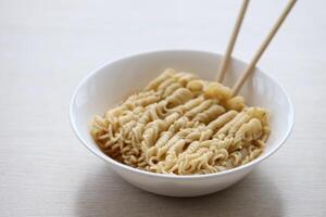 Bowl of instant cooking noodles with wooden chopsticks on white wooden table photo