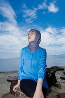 Muslim woman is sitting on the beach facing upwards, against the sky as a background with empty space for photocopying. photo