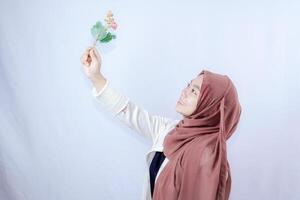 a veiled Javanese woman is looking at a flower held up in her hand against the background of an empty space for photocopying. photo