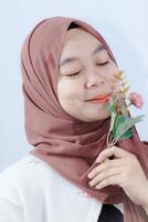 woman in hijab kissing plastic flowers on white background with empty space for photocopy. photo