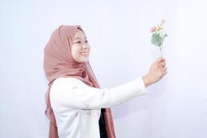 a veiled Javanese woman is looking at a flower held up in her hand against the background of an empty space for photocopying. photo