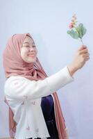 a veiled Javanese woman is looking at a flower held up in her hand against the background of an empty space for photocopying. photo