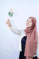 a veiled Javanese woman is looking at a flower held up in her hand against the background of an empty space for photocopying. photo