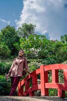 Muslim woman is standing on a bridge against a backdrop of trees with empty sky space for photocopying. photo
