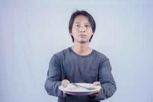 Portrait of Asian men who are hungry holding empty plates to ask to eat with a white background that is isolated for the photocopy space on it. Menu Poet Concept. photo