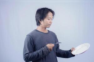 handsome asian man holding empty plate while thinking for serving food menu on isolated white background for advertising menu. menu presentation concept. photo