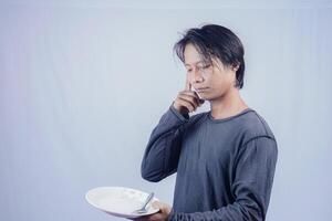 handsome asian man holding empty plate while thinking for serving food menu on isolated white background for advertising menu. menu presentation concept. photo