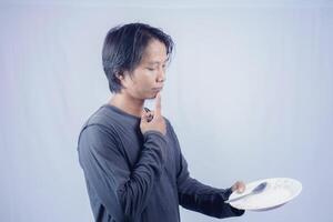 handsome asian man holding empty plate while thinking for serving food menu on isolated white background for advertising menu. menu presentation concept. photo